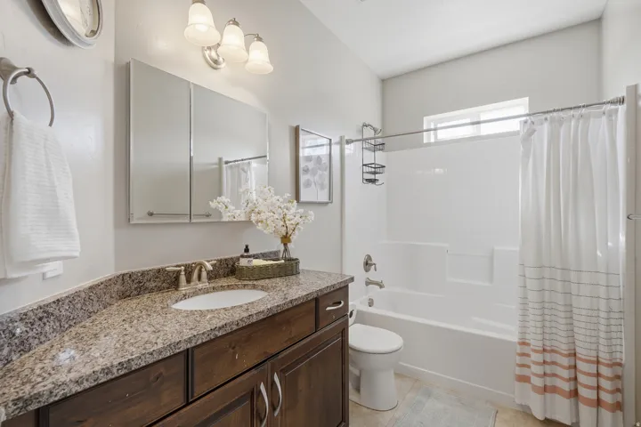 Granite-style countertop with an undermount sink, wood-finish cabinetry, built-in medicine cabinet, and a shower-tub combination with a window