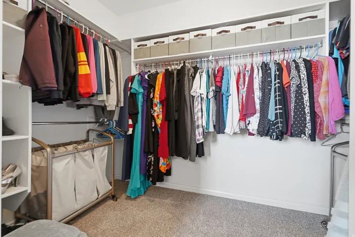 Walk-in closet featuring white built-in shelving, multiple hanging rods, and light gray carpeting