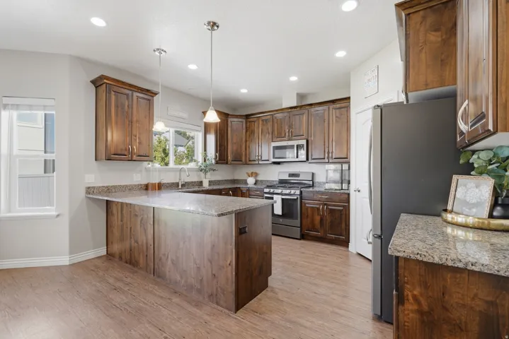 Spacious kitchen featuring wood-finish flooring, dark wood cabinetry, light speckled countertops, stainless steel appliances, and recessed lighting