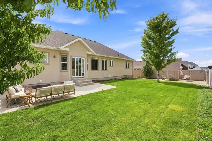 Expansive green lawn, concrete patio, multi-pane sliding glass door, multiple windows, and a privacy fence