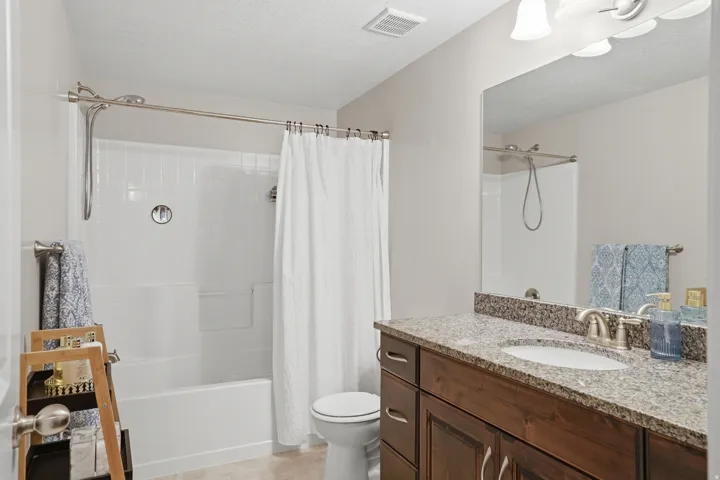 Bathroom featuring a single vanity with dark wood-finish cabinetry, a light-colored speckled countertop, an undermount sink, and a combination tub and shower