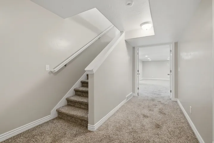 Carpeted staircase with white handrail and trim, leading to a hallway with recessed lighting and a neutral color palette