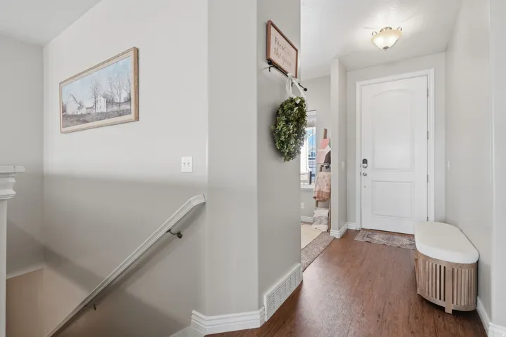 Warm-toned wood-finish flooring, white paneled entry door, and a built-in stair handrail