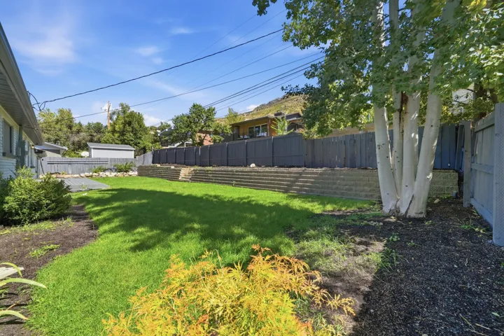 Expansive backyard featuring a manicured lawn, established perimeter fencing, and terraced landscaping