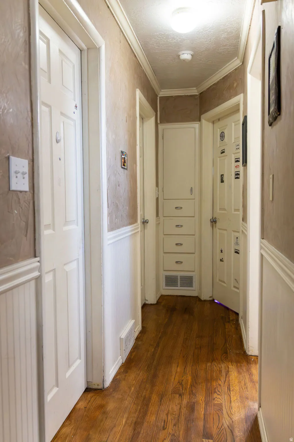 Hallway featuring wood-finish flooring, wainscoting, and crown molding