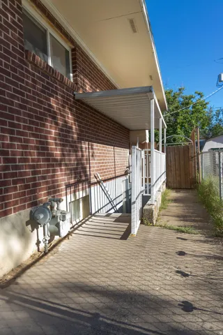 Brick exterior with a covered entry, concrete walkway, and a privacy fence