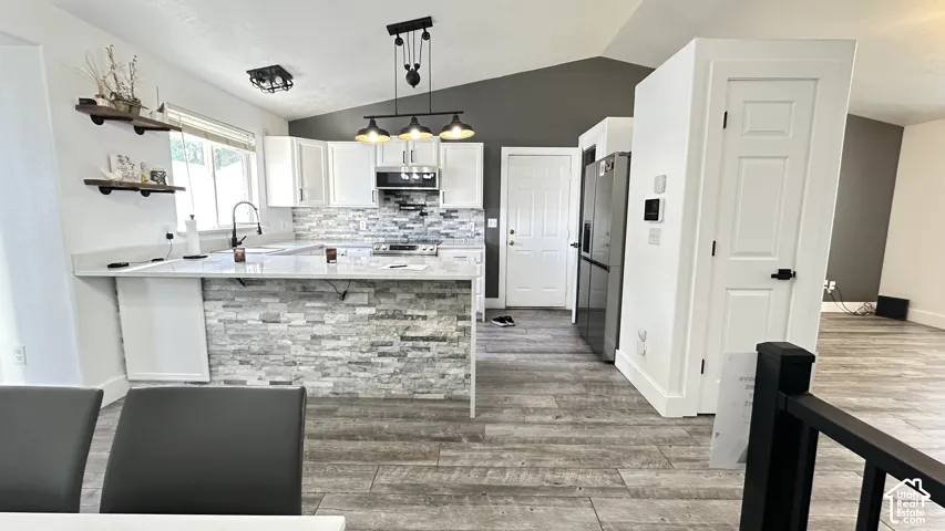 Bright, open-concept kitchen showcasing quartz countertops, a textured stone backsplash, tile flooring, crisp white cabinetry, and premium stainless-steel appliances. The expansive peninsula adds both functionality and style, creating an ideal space for e