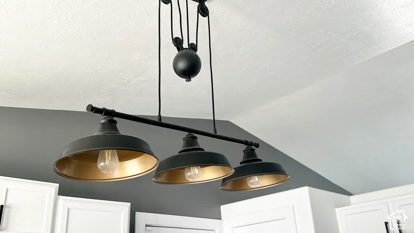 Industrial-style multi-light fixture with a pulley system, featuring three black metal shades with gold-finish interiors, recessed lighting, and white cabinetry