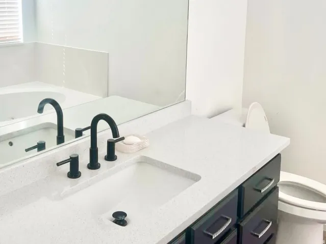 Master bath - Spacious vanity with an integrated sink, matte black fixtures, dark wood-finish cabinetry, and a white quartz ountertop