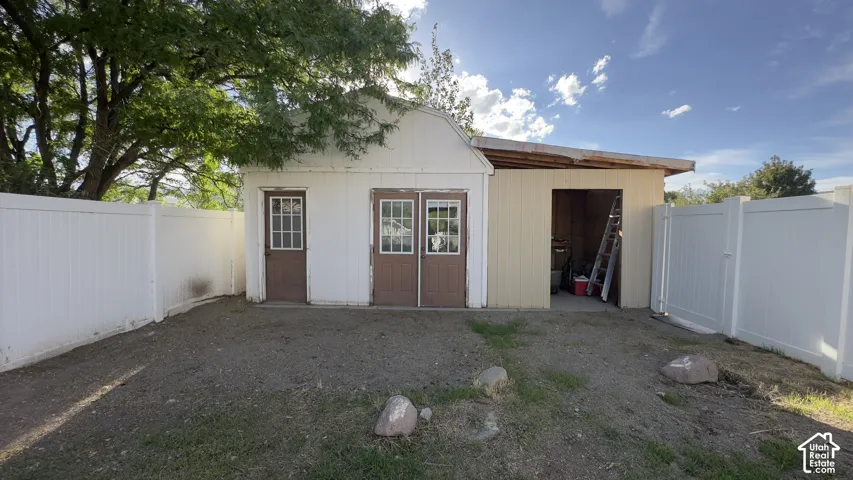 Designed with manicured lawn, concrete pathway, white privacy fencing, two-door outbuilding, and an open-sided storage structure