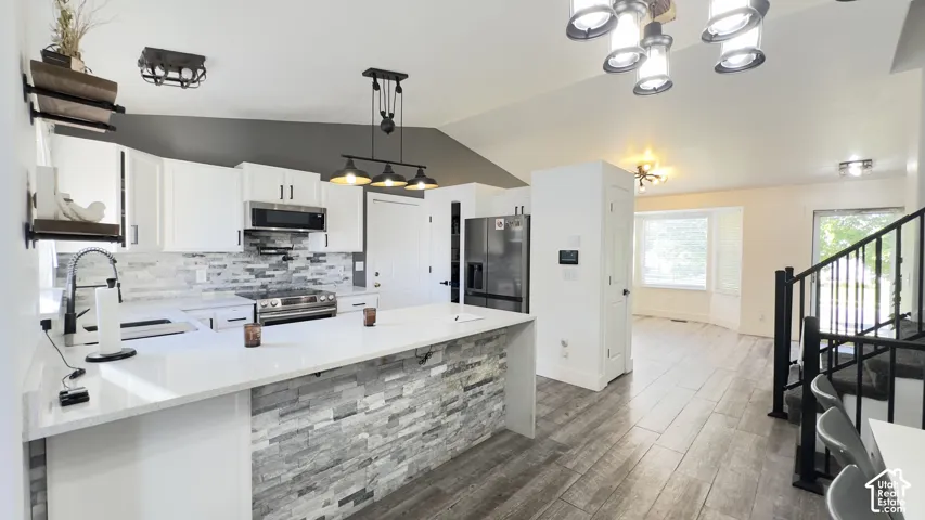 Beautifully updated kitchen featuring quartz countertops, stone backsplash, tile flooring, white cabinetry, and premium stainless-steel appliances. The oversized peninsula provides generous prep and entertaining space, while the open layout flows seamless