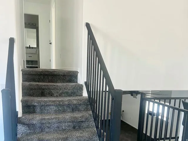 Carpeted staircase with black metal railings, leading to a hallway towards 3 bedrooms including the master bedroom and bath