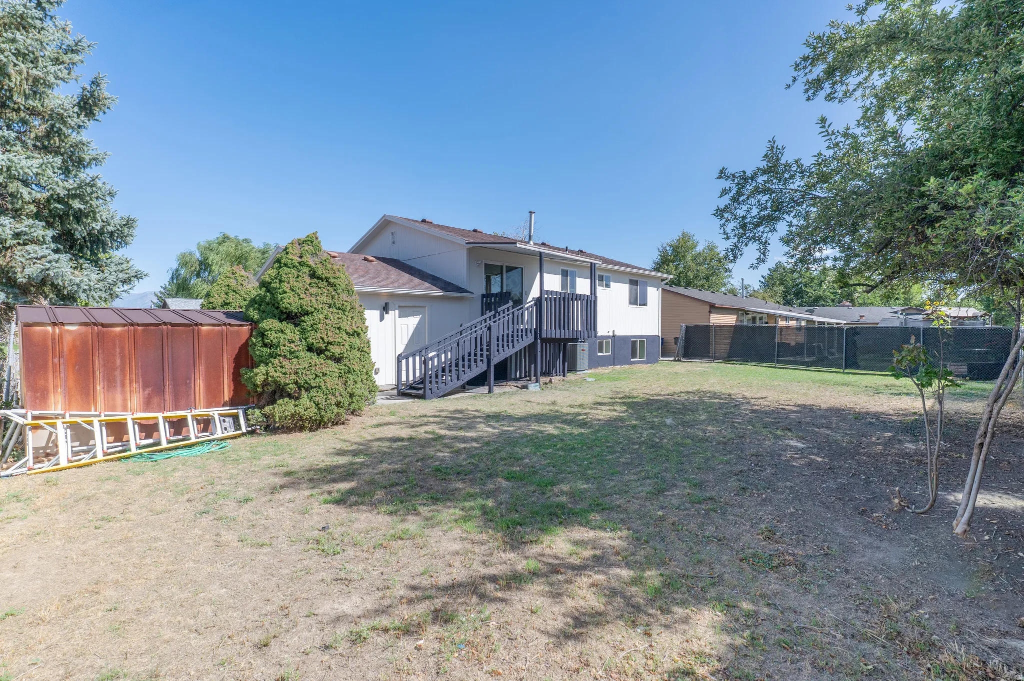 Expansive rear yard with mature perimeter trees, a multi-level deck, and a detached storage shed