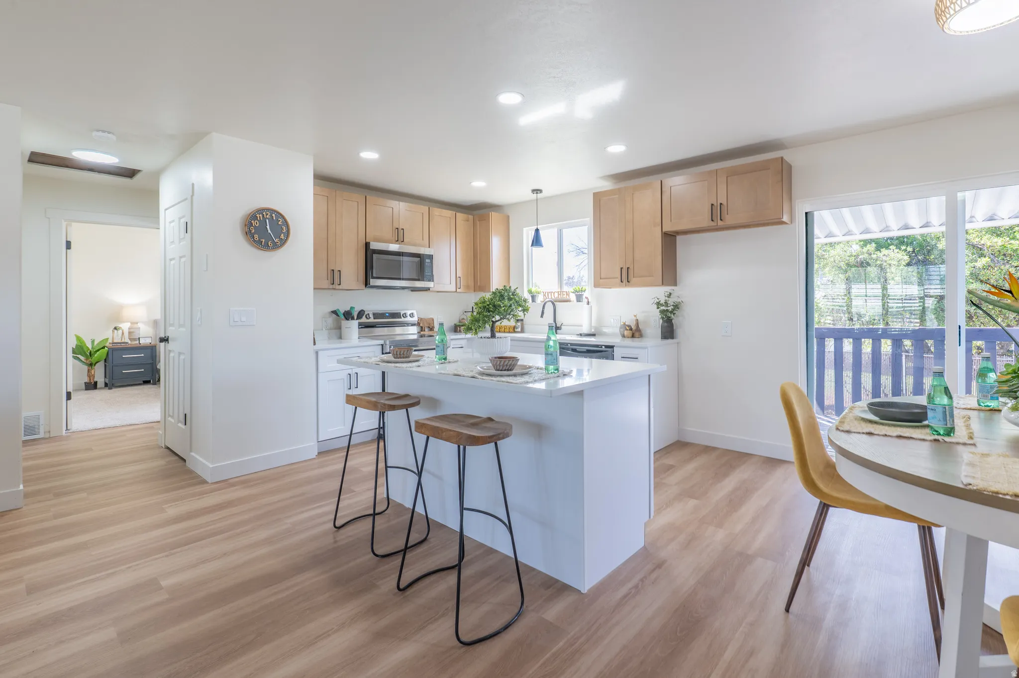 Kitchen featuring wood-finish flooring, recessed lighting, light wood cabinetry with dark hardware, a center island with countertop seating, and a sliding glass door to an outdoor area