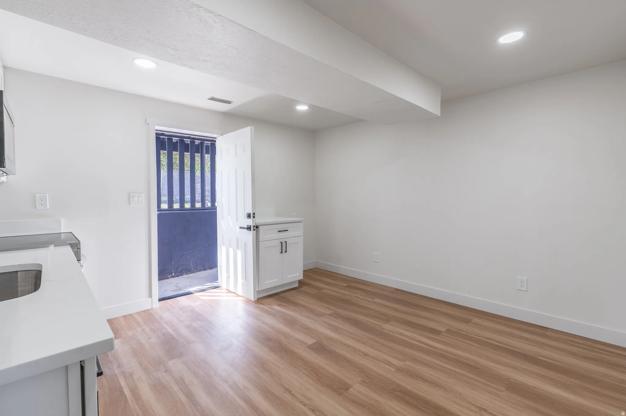 Hardwood-style flooring, recessed lighting, white cabinetry, quartz-style countertop, and a white entry door