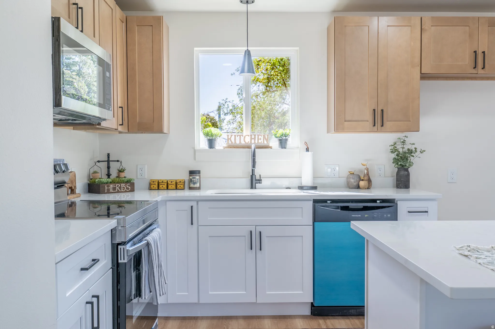 Kitchen featuring light wood-finish upper cabinetry, white lower cabinetry, stainless steel microwave, black electric range, and solid surface countertops