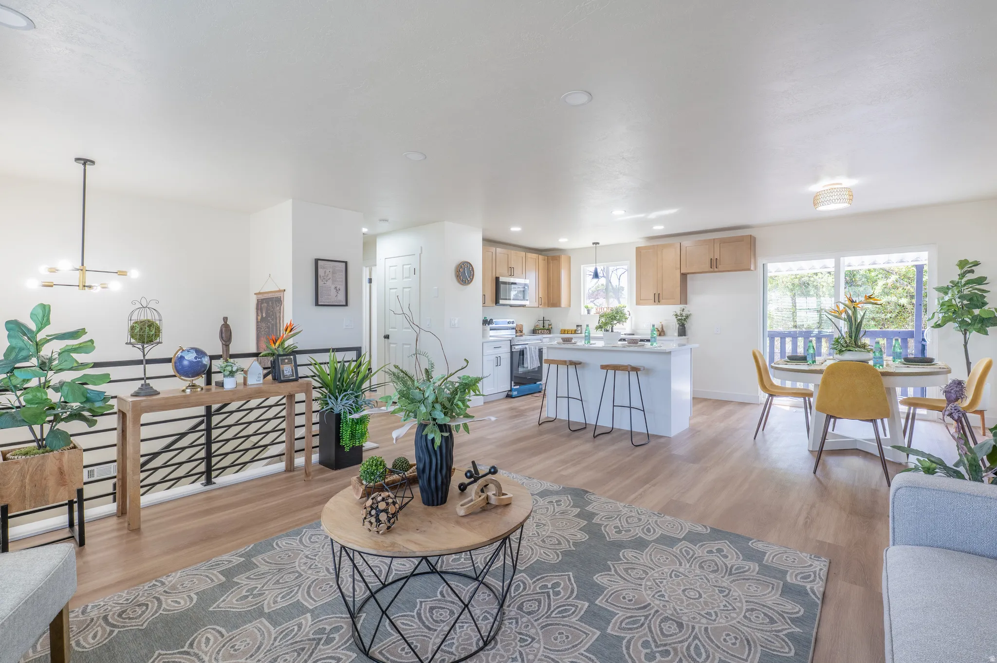 Spacious living area with wood-finish flooring, an open kitchen featuring light wood cabinetry, a breakfast bar with a white countertop, and a dining area with a large window