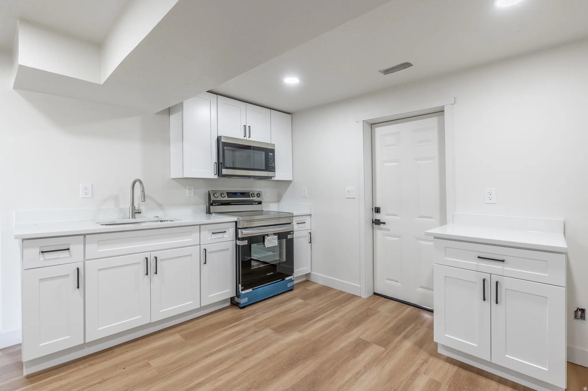 Modern kitchen featuring white shaker cabinetry, stainless steel appliances, light countertops, a stainless steel sink with a gooseneck faucet, and wood-finish flooring