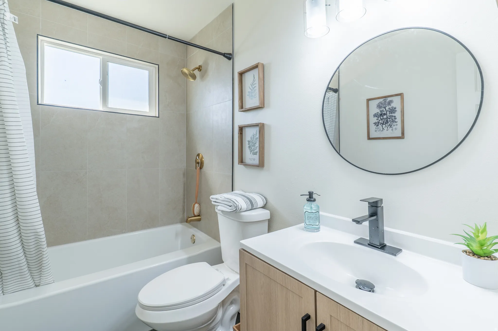 Built-in bathtub with subway tile surround, matte black faucet, wood-finish vanity with integrated sink, and circular vanity mirror