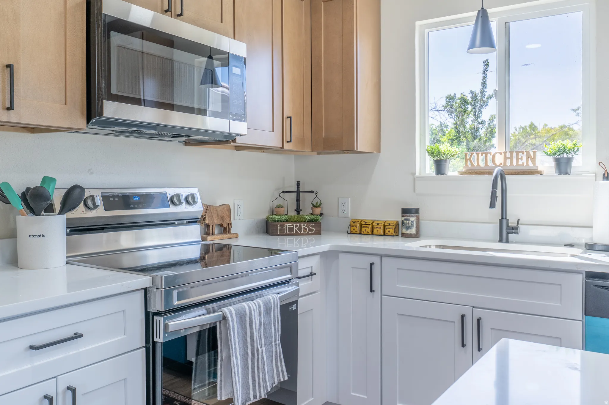 Stainless steel oven with an induction cooktop, light wood upper cabinetry, white lower cabinetry, and a stainless steel over-the-range microwave