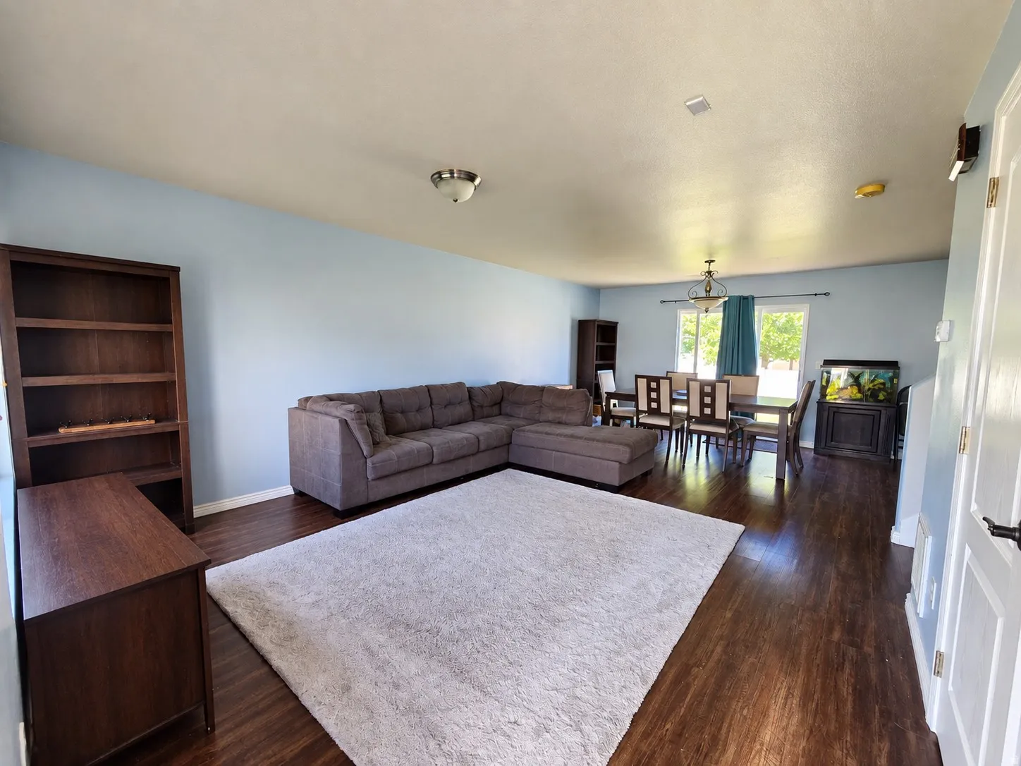 Open-concept living area featuring wood-finish flooring, light blue wall paint, and a dining space with a chandelier