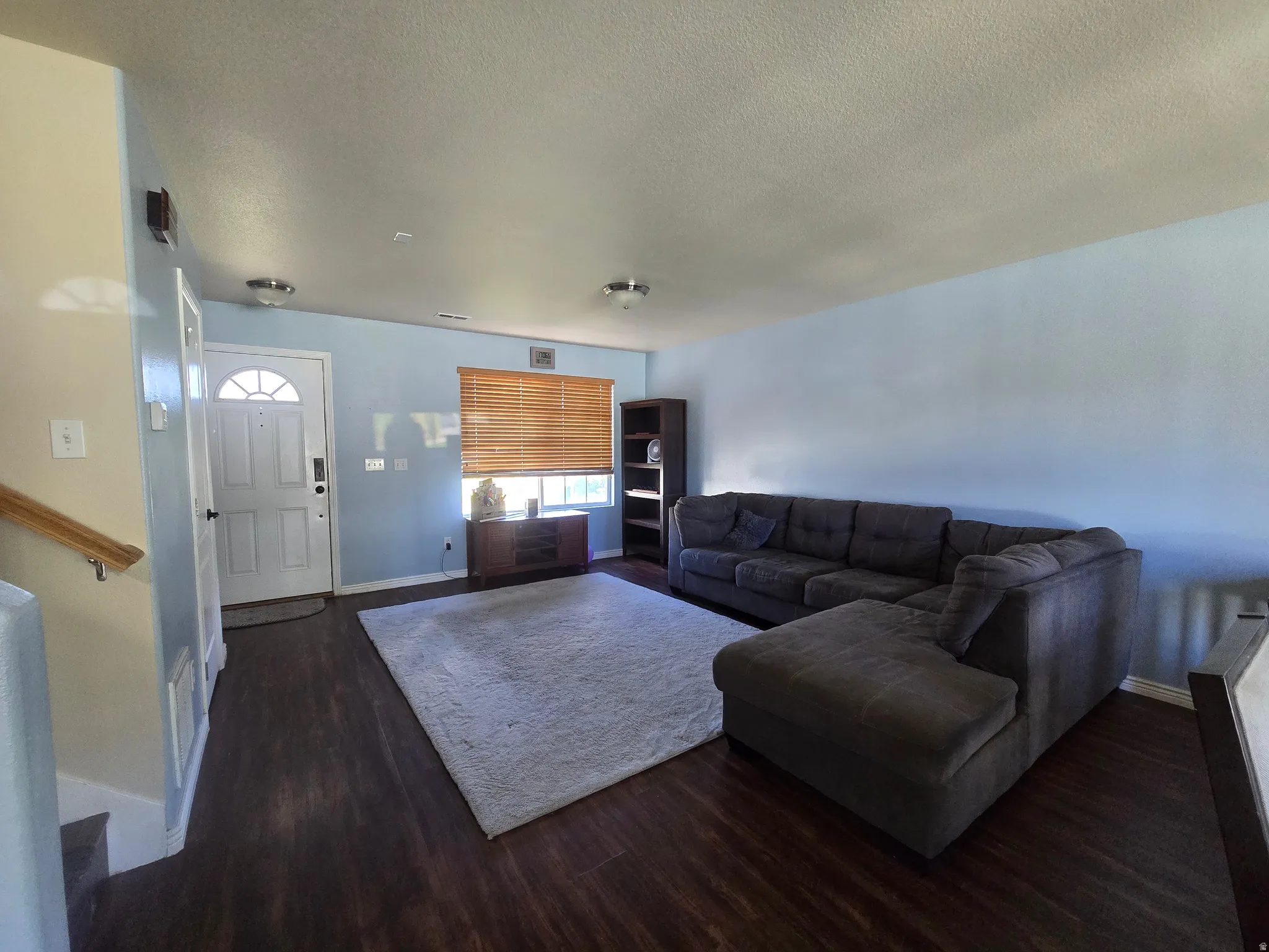 Wood-finish flooring throughout, featuring a paneled entry door with an arched lite, and a window with wood blinds