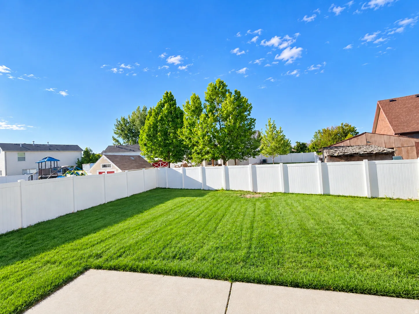 Expansive backyard featuring a manicured lawn, full white privacy fencing, and a concrete patio area