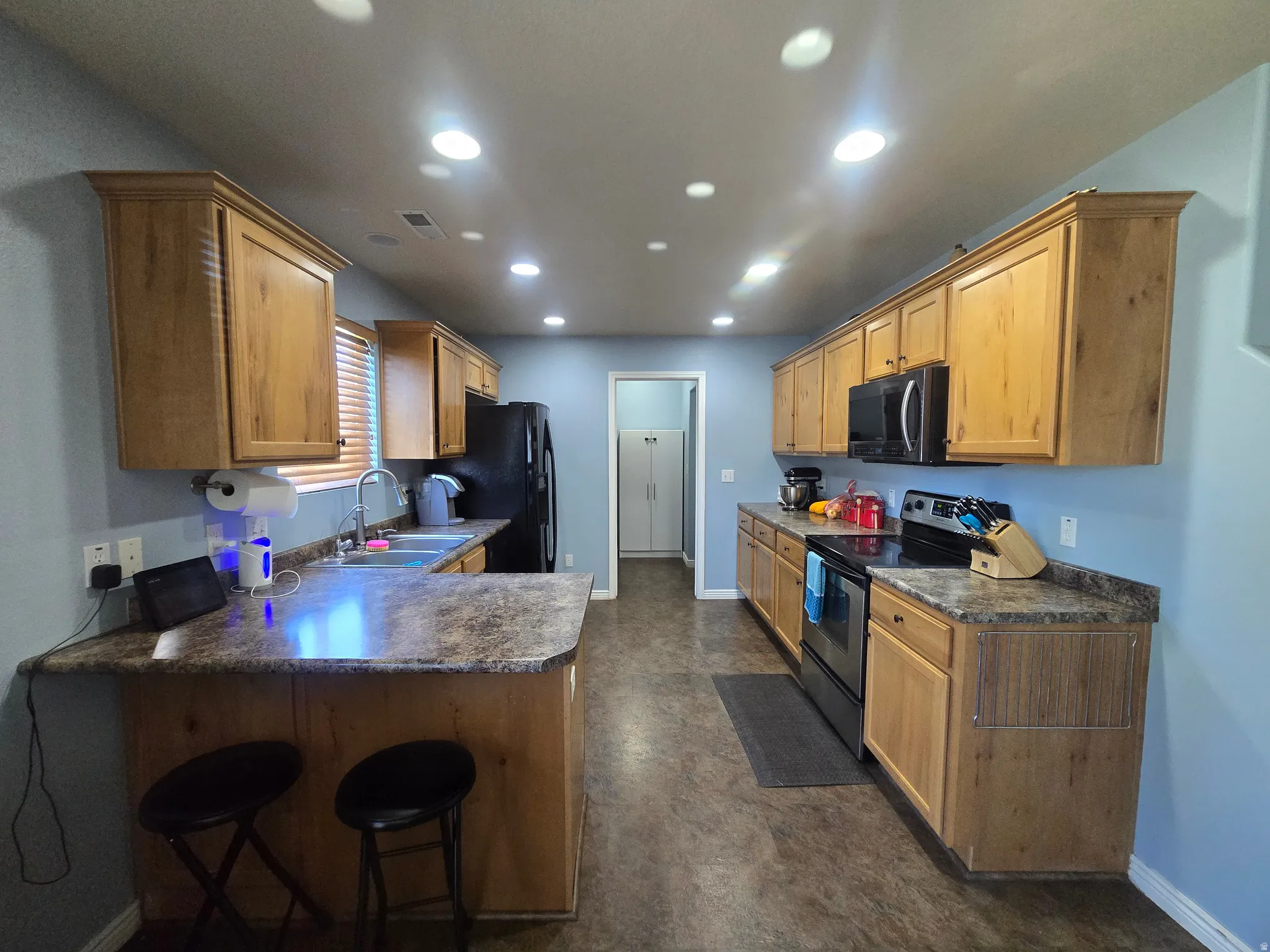 Kitchen featuring wood-finish cabinetry, dark countertops, stainless steel sink, black built-in microwave, and recessed lighting