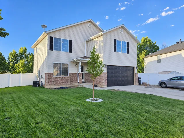 Two-story exterior with vinyl siding and brick detailing, featuring a two-car garage, front entry porch, and white privacy fencing