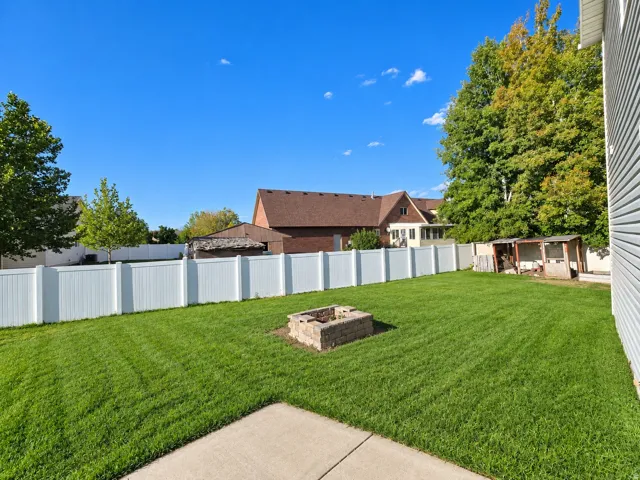Expansive green lawn featuring a stone fire pit, bordered by a white privacy fence, and a concrete patio section