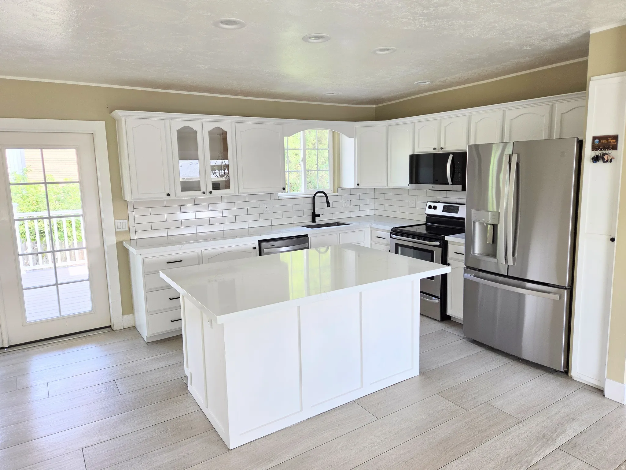 Modern kitchen featuring white cabinetry, stainless steel appliances, a center island with solid surface countertop, white subway tile backsplash, and wood-finish flooring