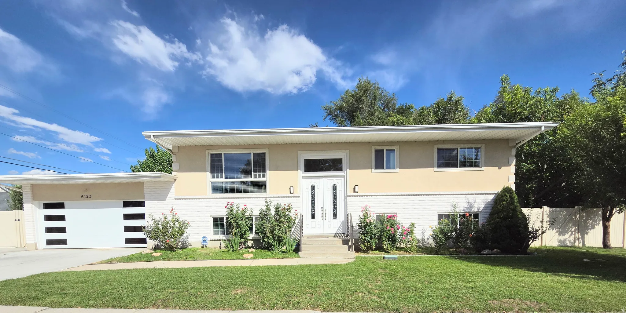 Two-story residence featuring a white brick and stucco exterior, an attached garage with contemporary horizontal window inserts, and a prominent front entry with double doors