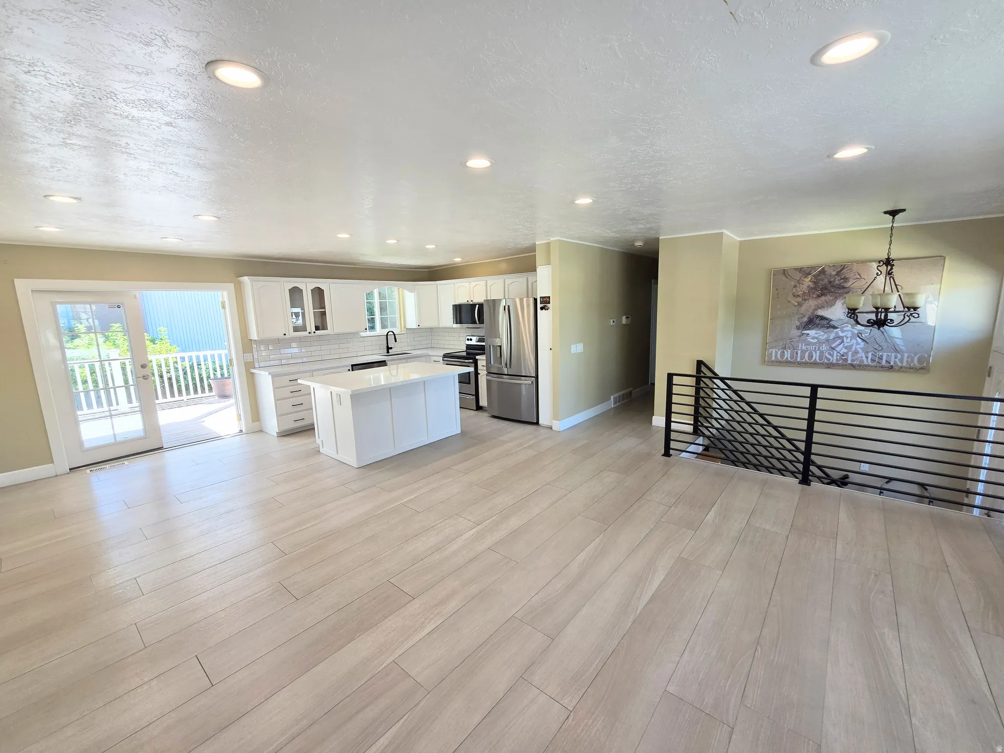 Spacious open-concept living area featuring light wood-finish flooring, a contemporary kitchen with white cabinetry, a central island, and stainless steel appliances