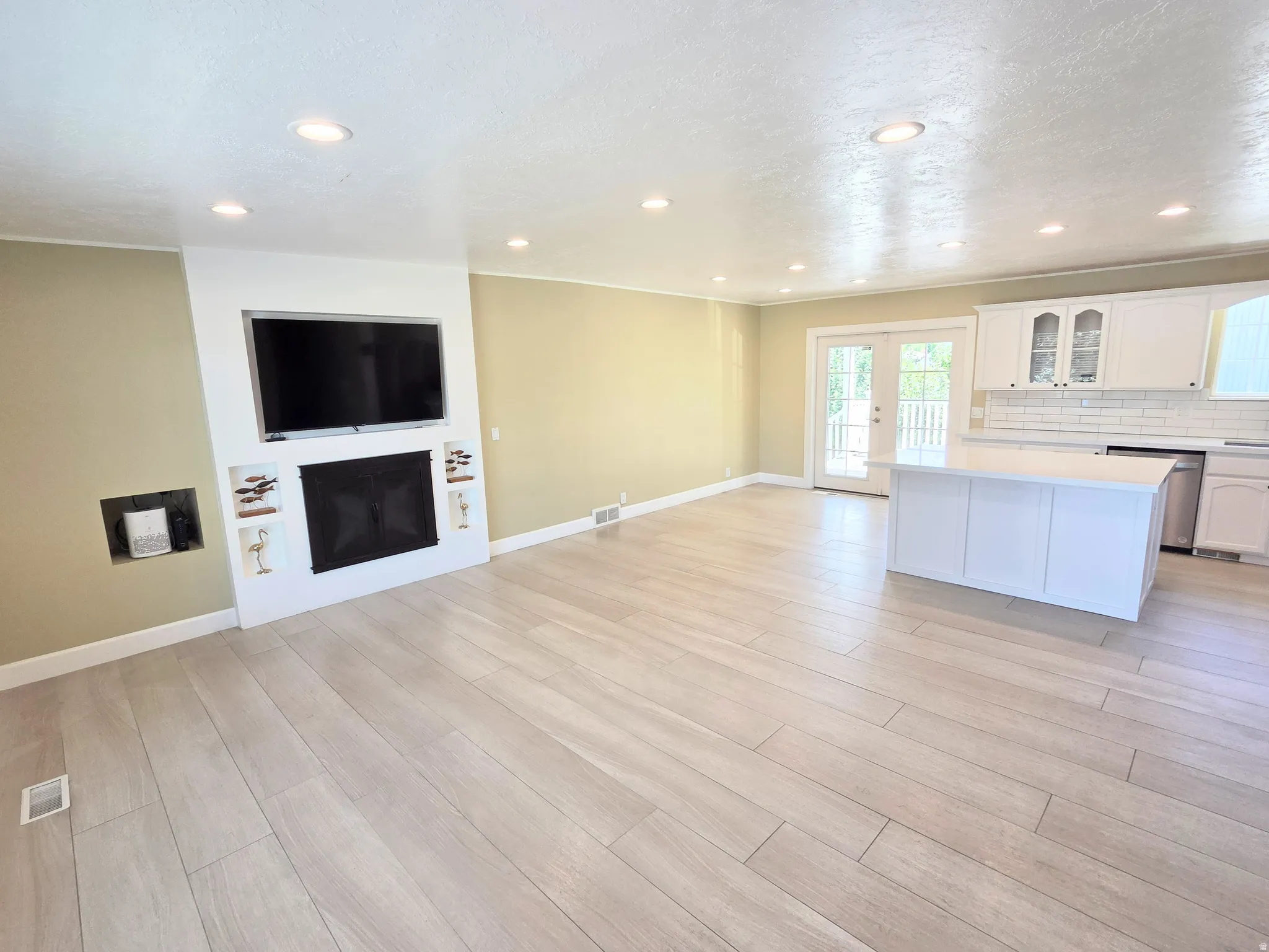 Open-concept living area featuring wood-finish flooring, recessed lighting, and a white fireplace surround