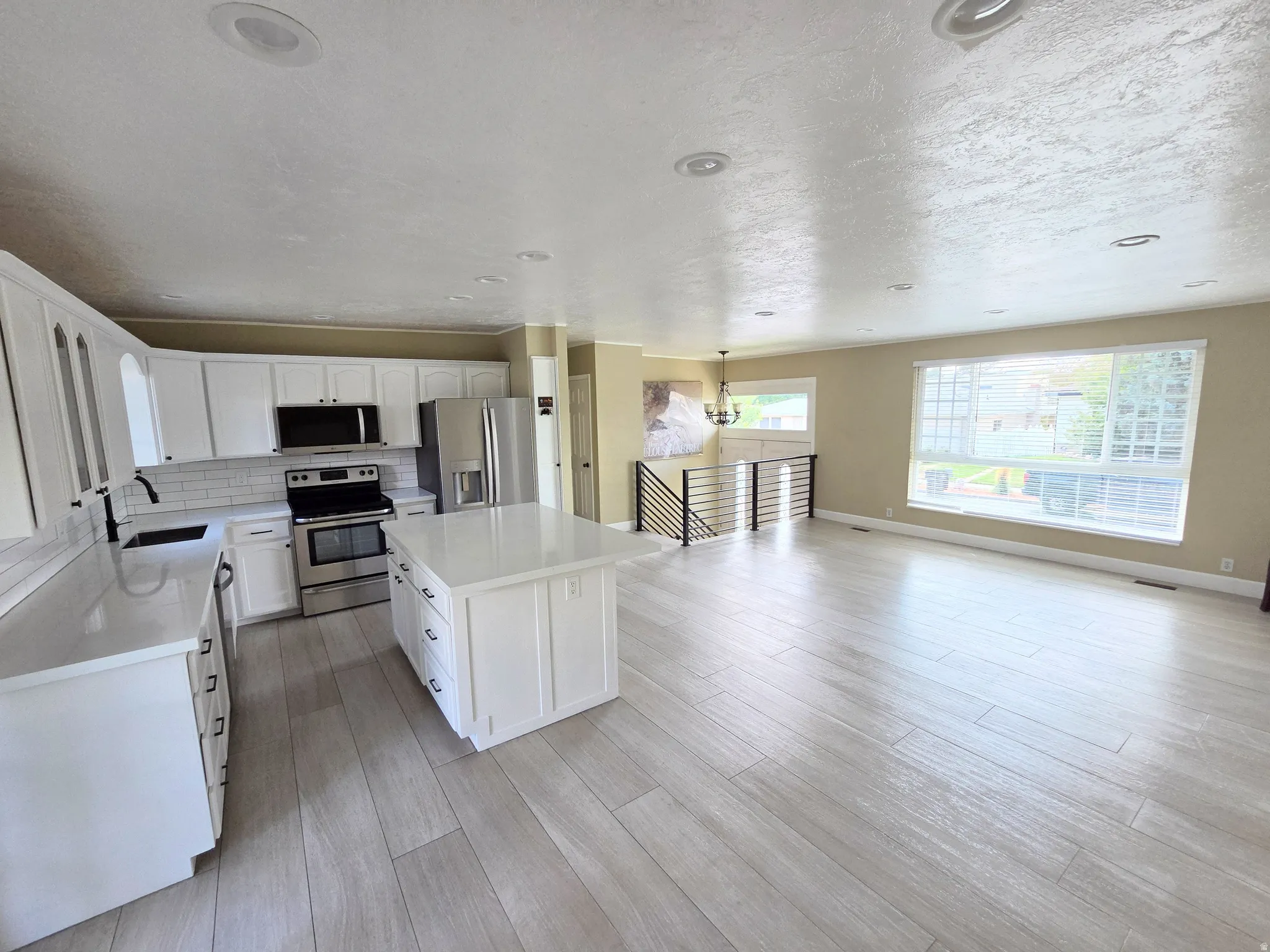 Open concept living space featuring a kitchen with white cabinetry and stainless steel appliances, a center island with a solid surface countertop, light wood-finish flooring, and recessed lighting