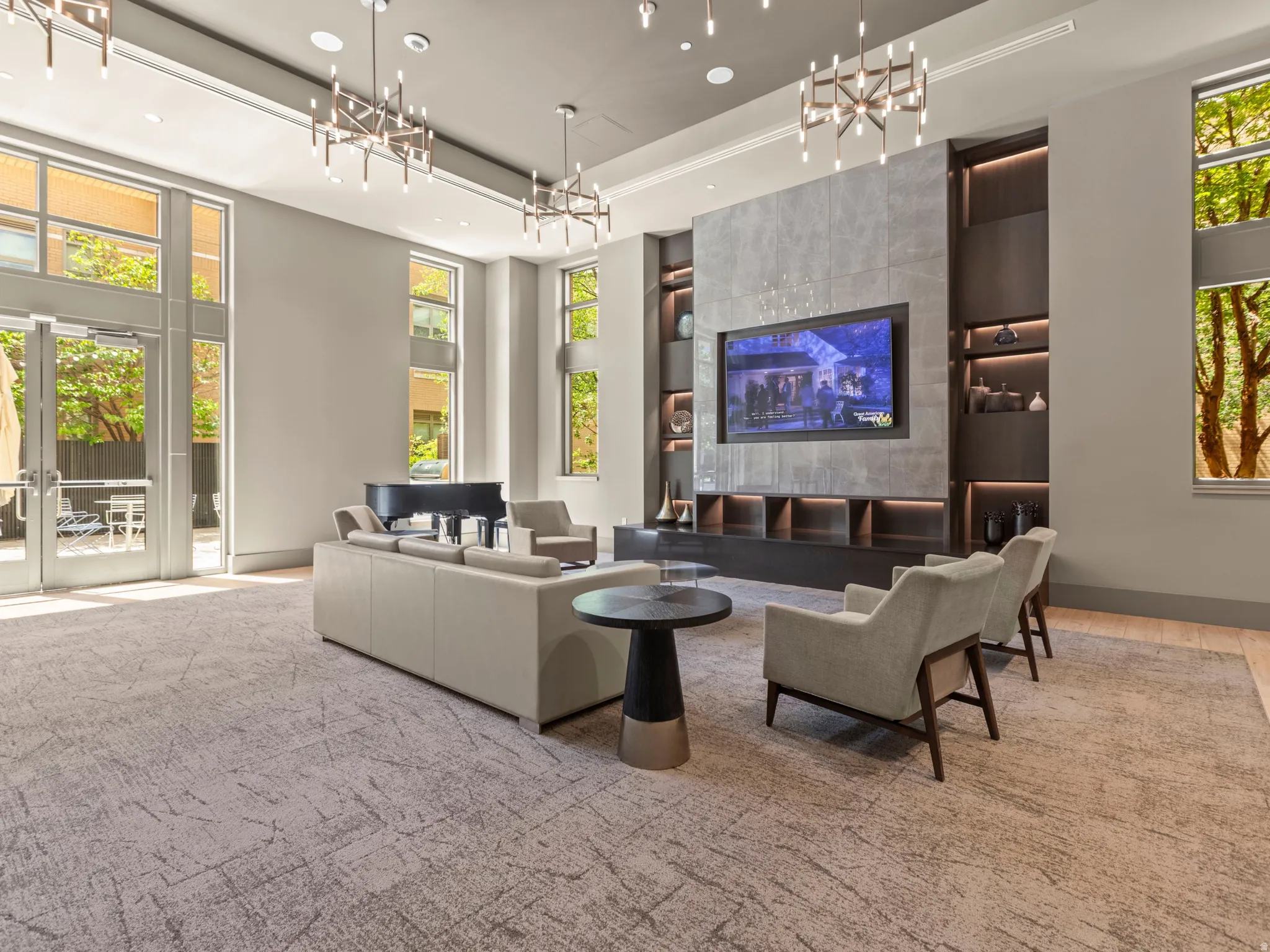 Spacious common area featuring large windows, multiple chandeliers, a built-in media console with shelving, and double glass doors
