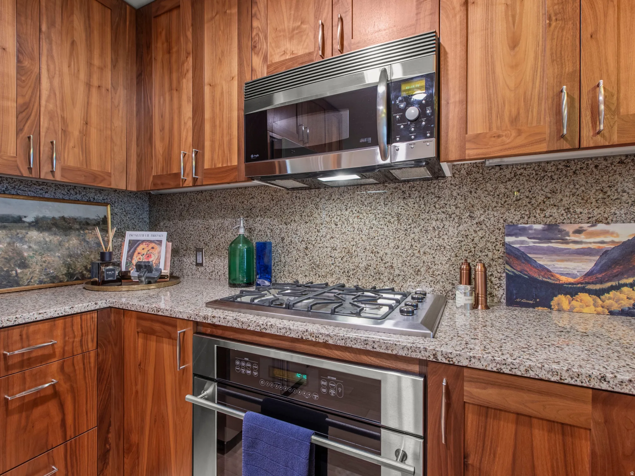 Wood cabinetry with brushed nickel hardware, granite countertops, integrated stainless steel oven, stainless steel microwave, and a gas cooktop