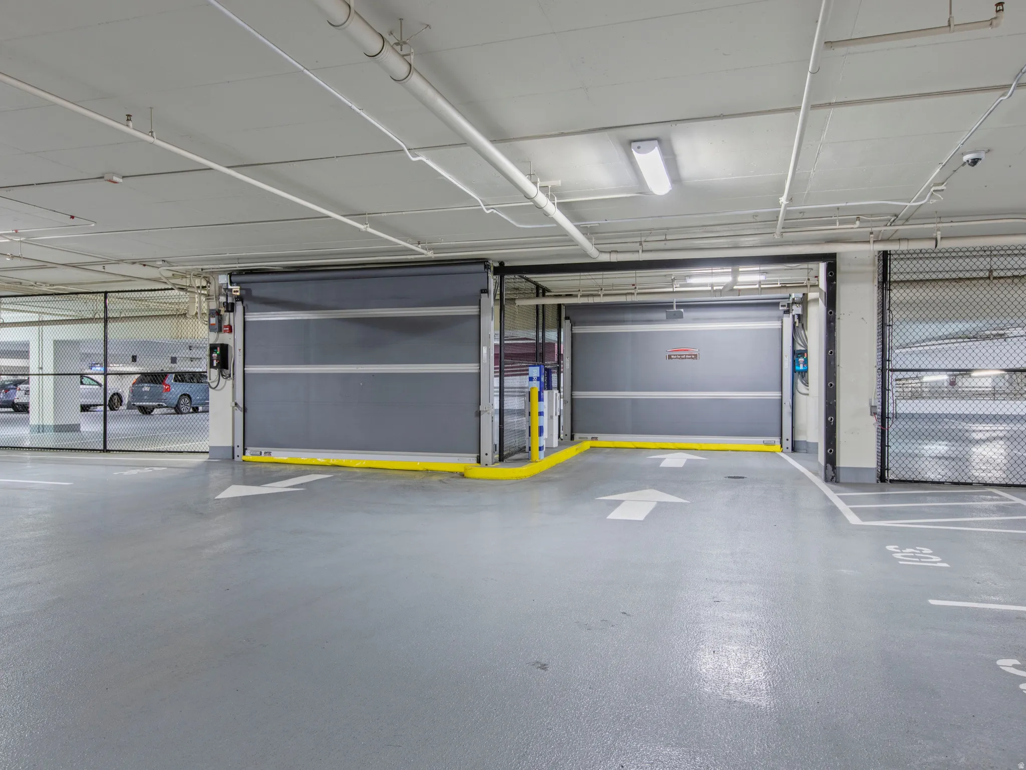 Secured Covered parking facility featuring two roll-up access doors, painted concrete flooring, and overhead fluorescent lighting