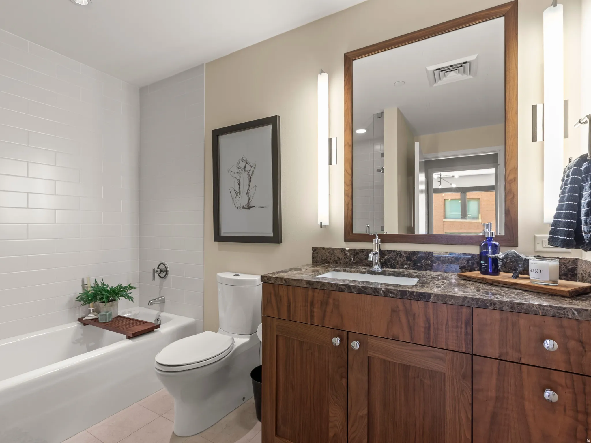 White subway tile bath surround, recessed lighting, wood-finish vanity with countertop, rectangular undermount sink, and wall-mounted mirror