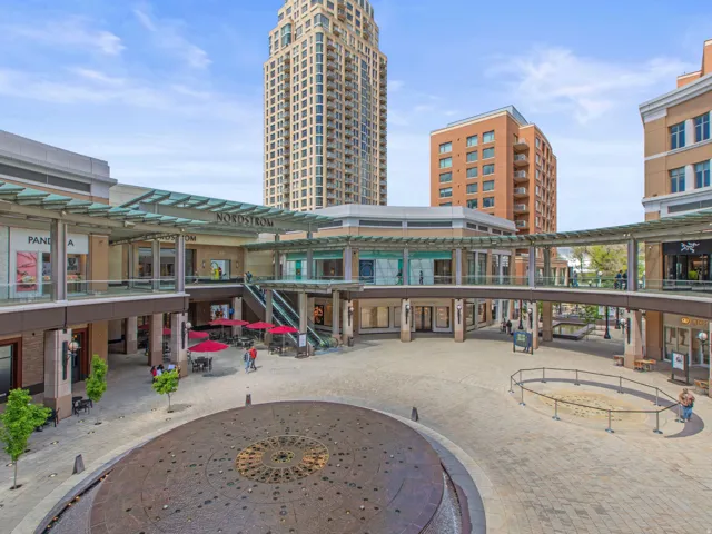 Multi-level commercial complex with ground-floor and upper-level retail spaces, featuring a central paved plaza and an ornate water feature