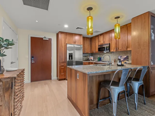 Kitchen featuring wood cabinetry, stainless steel appliances, a granite countertop island, and pendant lighting