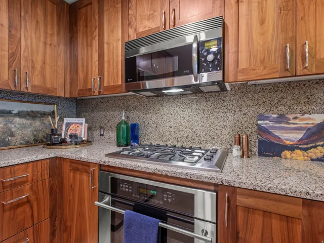 Wood cabinetry with brushed nickel hardware, granite countertops, integrated stainless steel oven, stainless steel microwave, and a gas cooktop