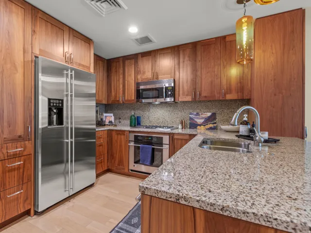 Wood-finish cabinetry, stainless steel appliances, speckled stone countertops, and a built-in kitchen sink