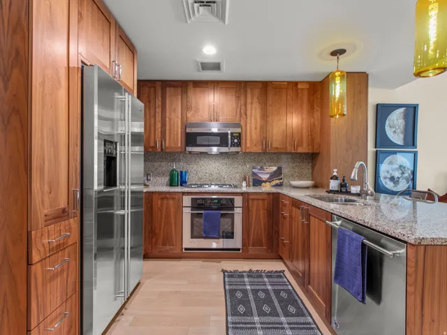 Kitchen featuring wood cabinetry, stainless steel appliances, speckled countertops, and a tile backsplash