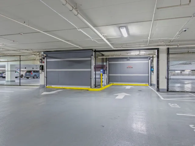 Secured Covered parking facility featuring two roll-up access doors, painted concrete flooring, and overhead fluorescent lighting