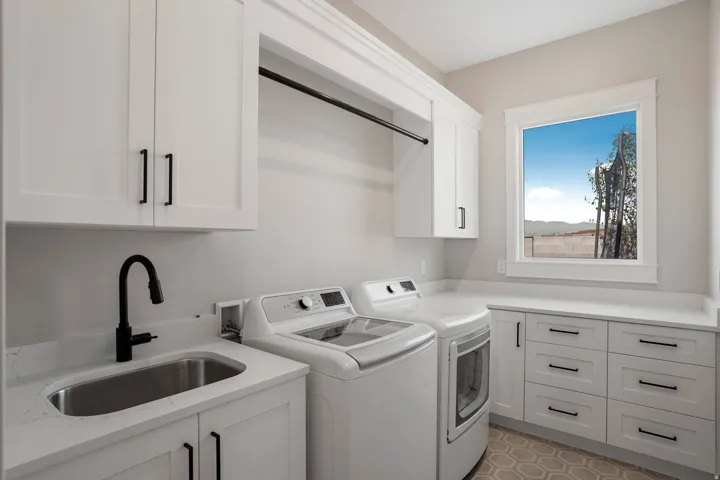 White shaker-style cabinetry, matte black hardware, integrated utility sink with a high-arch faucet, hexagonal floor tile, and a large window