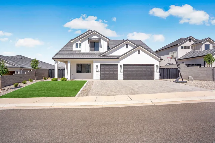 Modern stucco exterior with a multi-level roofline, brick paver driveway, and an attached two-car garage