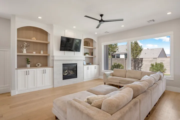 Recessed lighting illuminates wood-finish flooring, built-in shelving with arched accents, and a fireplace with a light-toned tile surround