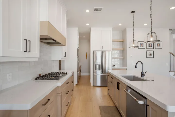 Kitchen featuring white upper cabinetry, wood-finish lower cabinetry, white countertops, stainless steel appliances, and pendant lighting