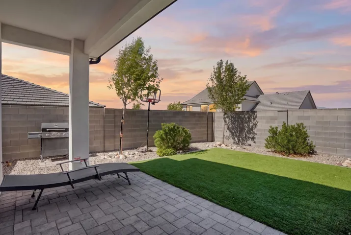 Covered patio with paver flooring, artificial turf, perimeter block wall, and gravel landscaping